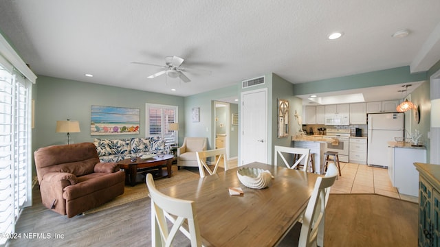 dining space with a textured ceiling, light wood-type flooring, and ceiling fan