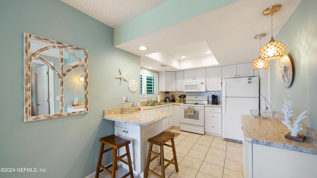 kitchen featuring white appliances, a kitchen breakfast bar, kitchen peninsula, light stone counters, and white cabinetry