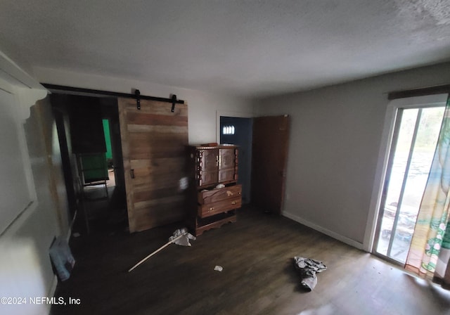 interior space featuring dark wood-type flooring, a barn door, access to exterior, and a textured ceiling