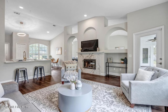 living room featuring a high end fireplace, hardwood / wood-style flooring, ceiling fan, and vaulted ceiling