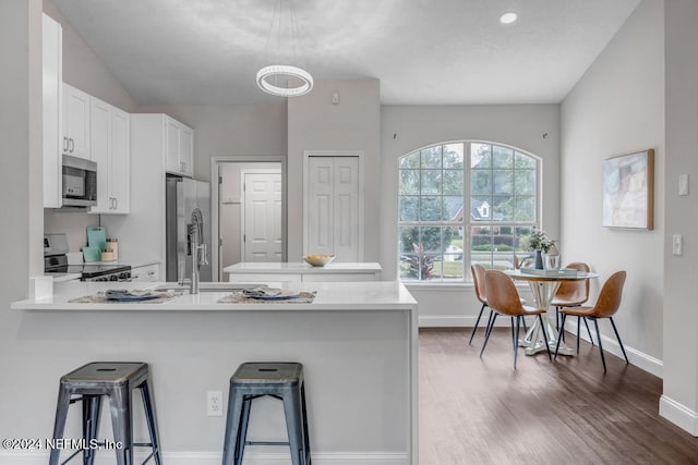 kitchen with a kitchen bar, kitchen peninsula, stainless steel appliances, white cabinets, and dark wood-type flooring