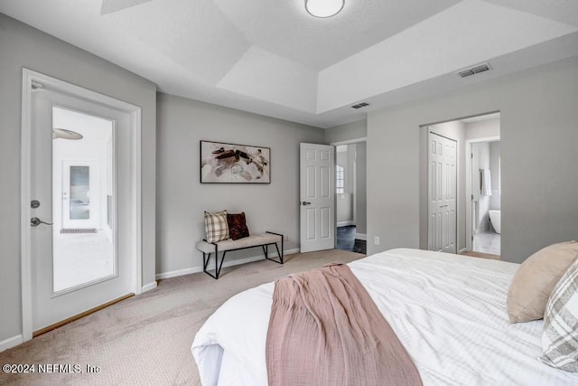 carpeted bedroom featuring ensuite bathroom and a raised ceiling