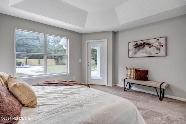 carpeted bedroom with access to outside and a tray ceiling