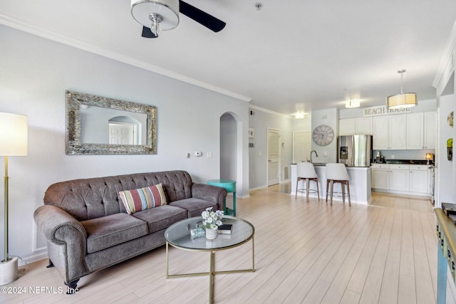 living room with ceiling fan, ornamental molding, sink, and light wood-type flooring