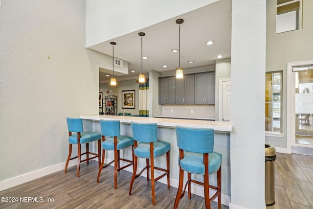 kitchen featuring gray cabinets, a breakfast bar, dark wood-type flooring, and pendant lighting