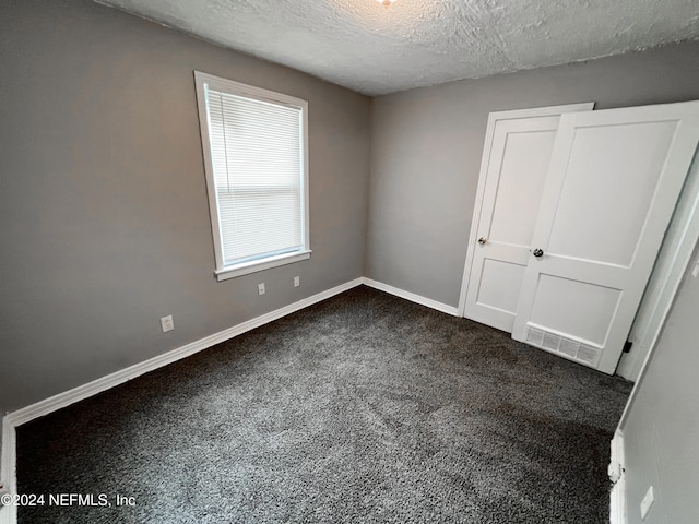 unfurnished bedroom with a textured ceiling and dark colored carpet