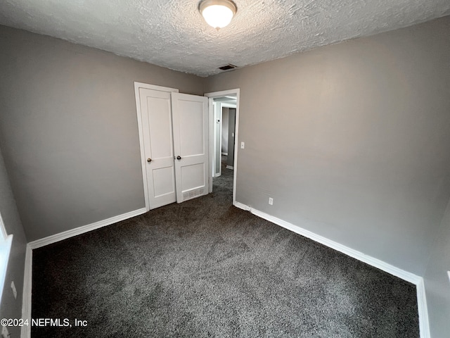 unfurnished bedroom with a textured ceiling and dark colored carpet