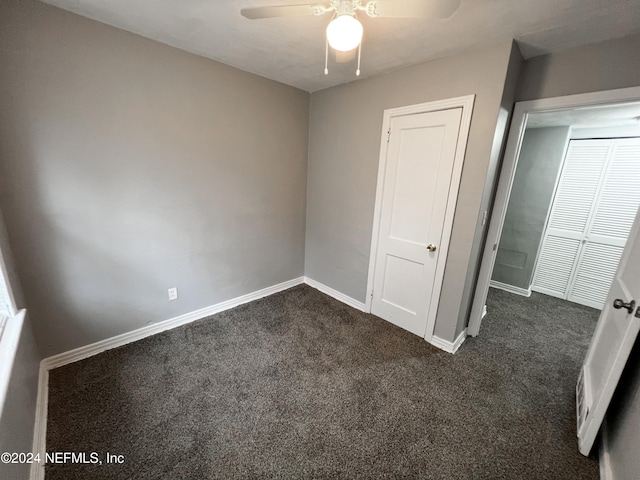 unfurnished bedroom with dark colored carpet, a closet, and ceiling fan