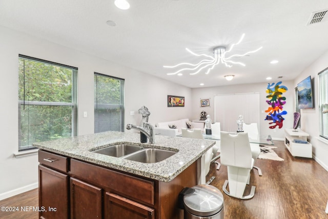 kitchen with a kitchen island with sink, dark hardwood / wood-style flooring, sink, and light stone counters