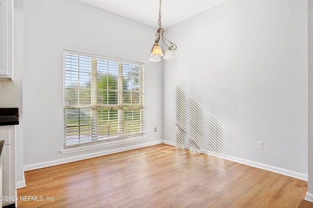 unfurnished dining area featuring a healthy amount of sunlight, a chandelier, and hardwood / wood-style floors