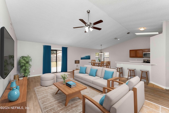 living room with a textured ceiling, light wood-type flooring, ceiling fan, and vaulted ceiling