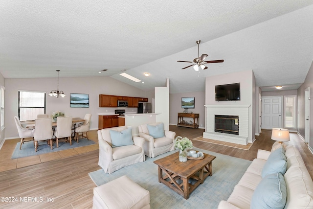 living room featuring light hardwood / wood-style floors, ceiling fan with notable chandelier, a textured ceiling, and vaulted ceiling