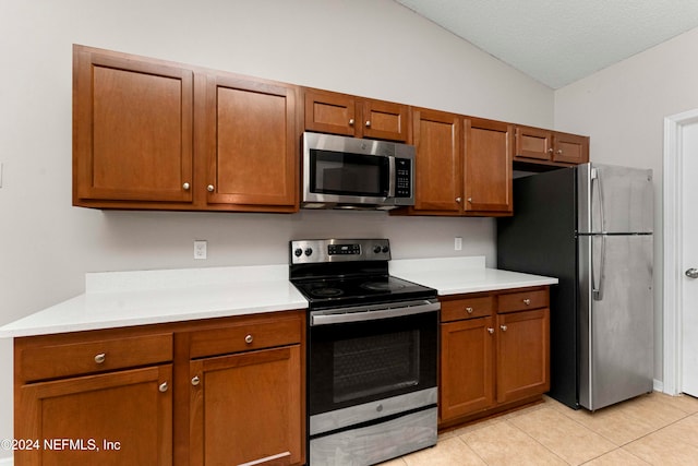 kitchen featuring a textured ceiling, appliances with stainless steel finishes, lofted ceiling, and light tile patterned floors