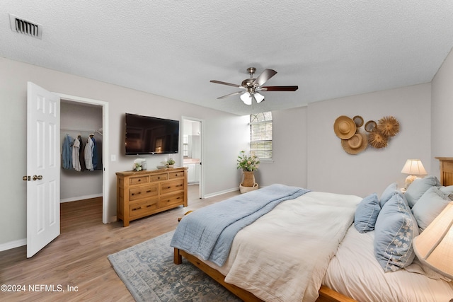 bedroom featuring light hardwood / wood-style floors, a textured ceiling, ensuite bathroom, ceiling fan, and a closet