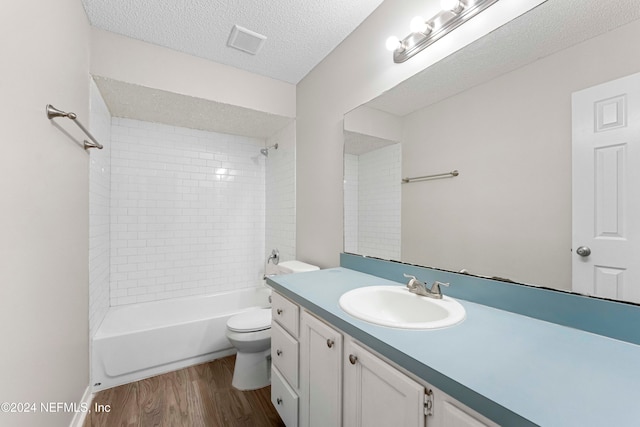 full bathroom with a textured ceiling, hardwood / wood-style floors, vanity, toilet, and tiled shower / bath combo