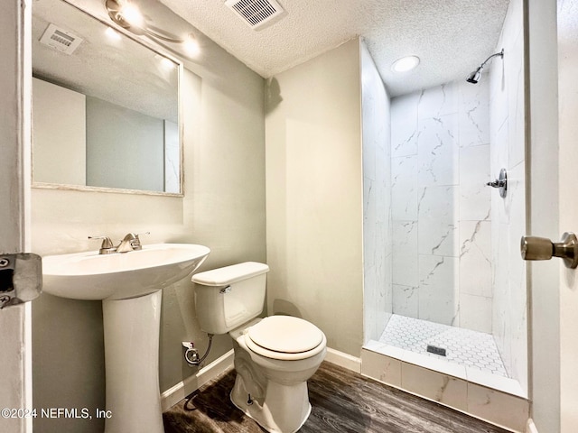 bathroom featuring a tile shower, a textured ceiling, toilet, and wood-type flooring