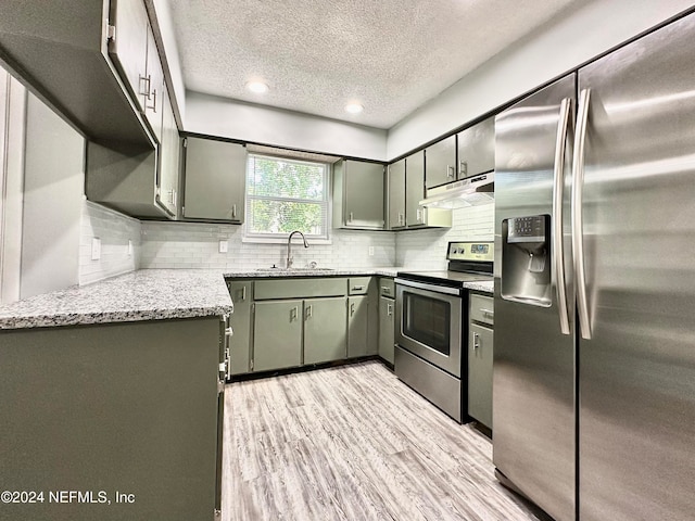 kitchen with sink, a textured ceiling, light hardwood / wood-style floors, stainless steel appliances, and light stone counters