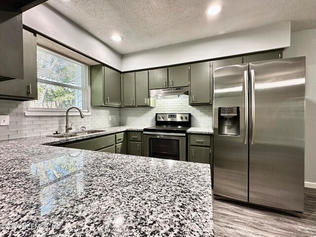 kitchen with decorative backsplash, light stone counters, appliances with stainless steel finishes, light hardwood / wood-style floors, and sink