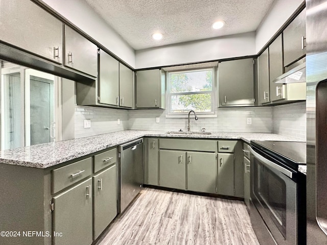 kitchen with appliances with stainless steel finishes, sink, a textured ceiling, light hardwood / wood-style floors, and ventilation hood