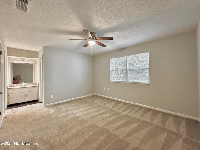 unfurnished bedroom featuring carpet floors, ensuite bathroom, a textured ceiling, and ceiling fan