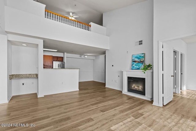 unfurnished living room featuring ceiling fan, a high ceiling, and light wood-type flooring