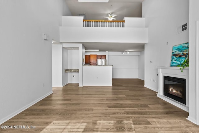 unfurnished living room featuring ceiling fan, a high ceiling, and hardwood / wood-style floors