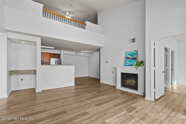 unfurnished living room with light hardwood / wood-style floors, a high ceiling, and ceiling fan