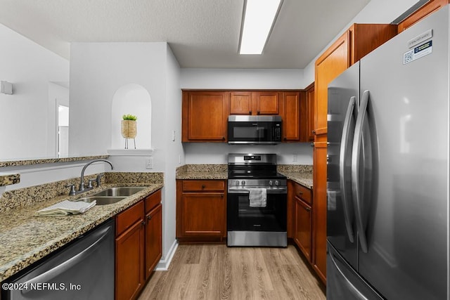 kitchen with sink, light stone countertops, stainless steel appliances, and light wood-type flooring