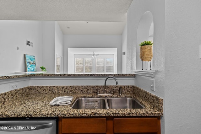 kitchen featuring sink, a textured ceiling, ceiling fan, dark stone counters, and stainless steel dishwasher