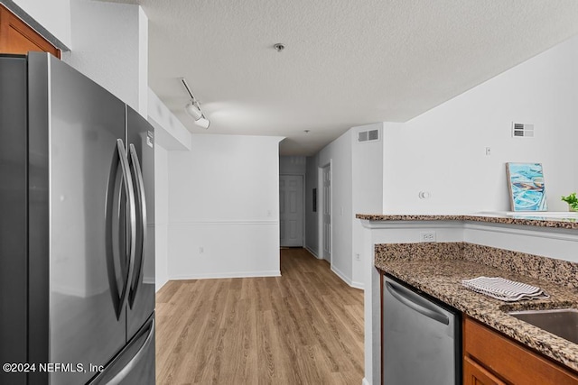 kitchen with track lighting, light hardwood / wood-style flooring, dark stone counters, appliances with stainless steel finishes, and a textured ceiling