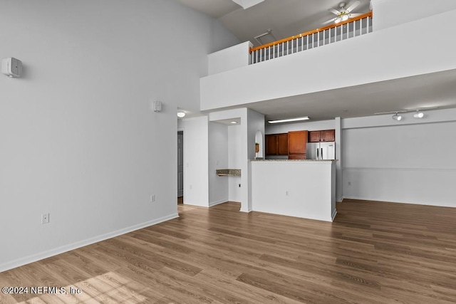 unfurnished living room featuring hardwood / wood-style floors, a high ceiling, and ceiling fan