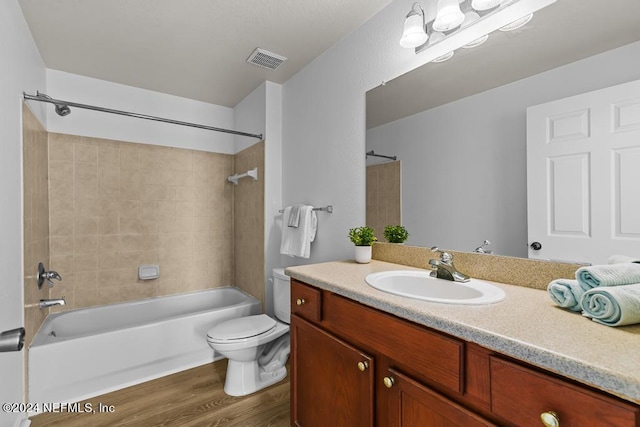 full bathroom with tiled shower / bath, vanity, hardwood / wood-style flooring, and toilet