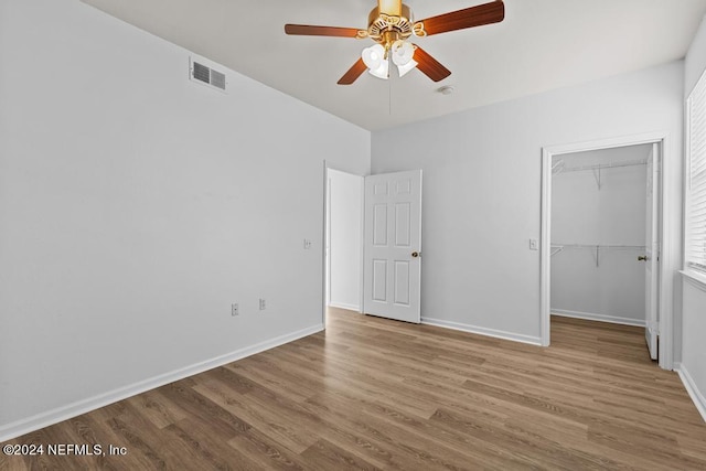 unfurnished bedroom with a walk in closet, a closet, light wood-type flooring, and ceiling fan