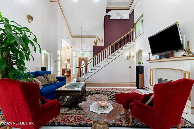 living room featuring ornamental molding, wood-type flooring, a tile fireplace, and a high ceiling