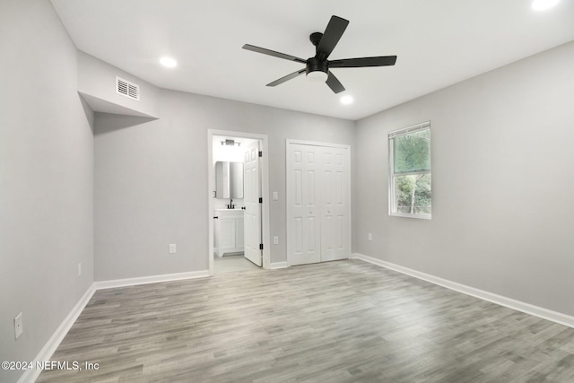 unfurnished bedroom featuring a closet, light hardwood / wood-style flooring, ensuite bathroom, and ceiling fan