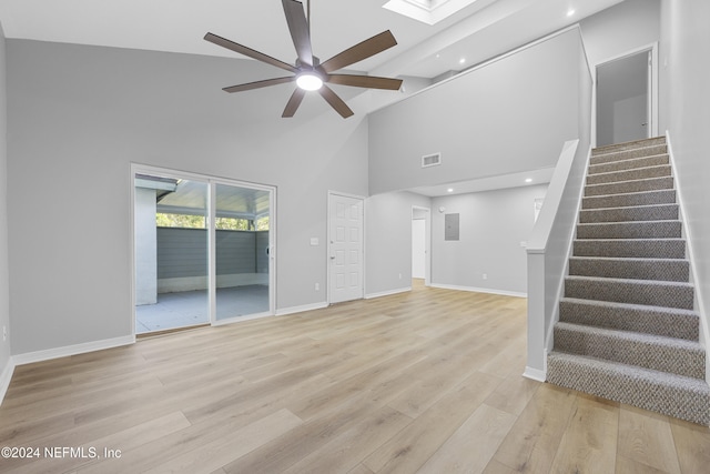 unfurnished living room featuring light hardwood / wood-style flooring, high vaulted ceiling, a skylight, and ceiling fan