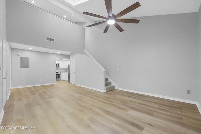 unfurnished living room with electric panel, light hardwood / wood-style floors, a high ceiling, ceiling fan, and a skylight