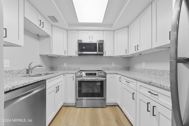 kitchen with sink, appliances with stainless steel finishes, white cabinets, and light hardwood / wood-style floors