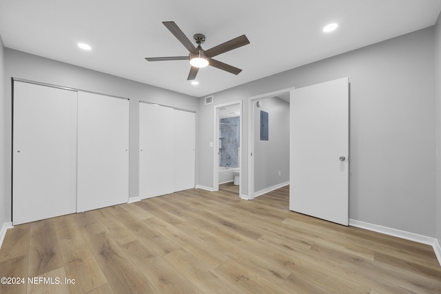 unfurnished bedroom featuring light hardwood / wood-style flooring, ensuite bath, electric panel, ceiling fan, and two closets