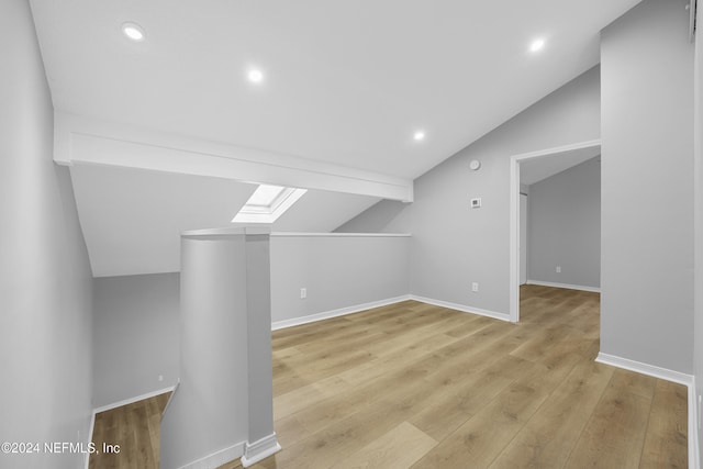 additional living space with vaulted ceiling with skylight and light hardwood / wood-style flooring