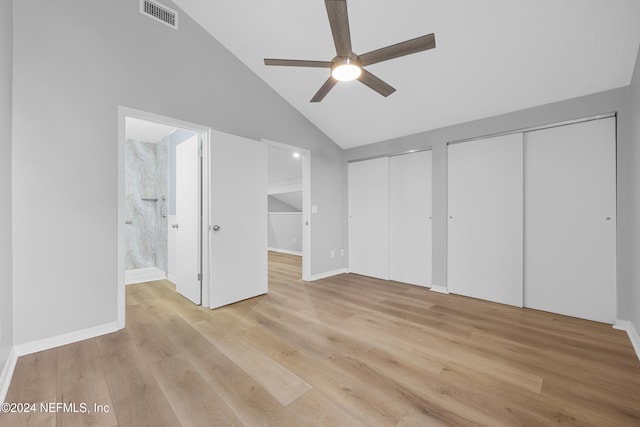 unfurnished bedroom featuring light wood-type flooring, lofted ceiling, ensuite bath, and two closets