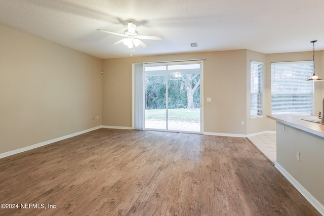 unfurnished living room with a textured ceiling, light hardwood / wood-style flooring, and ceiling fan