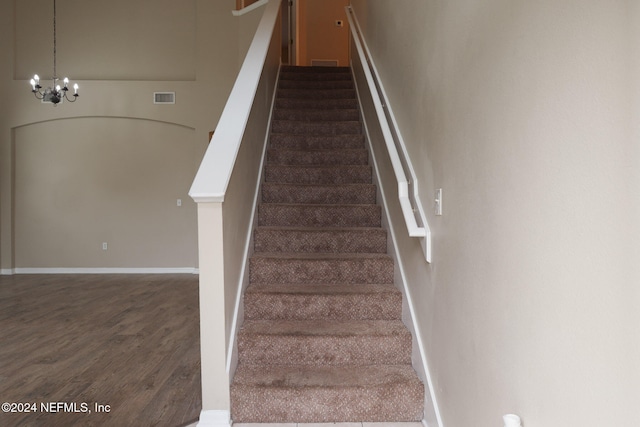 staircase with hardwood / wood-style floors and an inviting chandelier