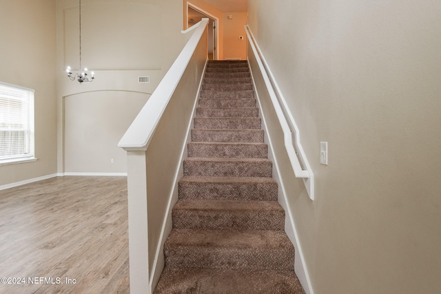 stairway with hardwood / wood-style floors and a notable chandelier