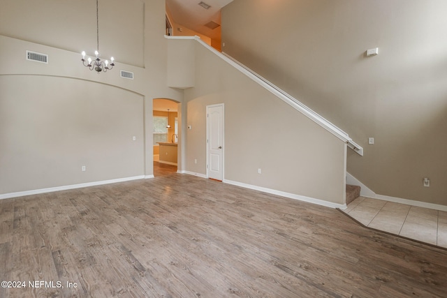 unfurnished living room with wood-type flooring, high vaulted ceiling, and a notable chandelier