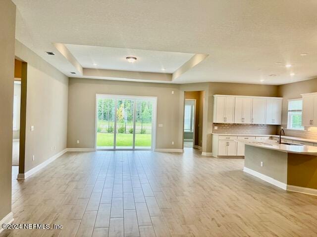 kitchen with light hardwood / wood-style floors, a kitchen island with sink, white cabinets, and a healthy amount of sunlight