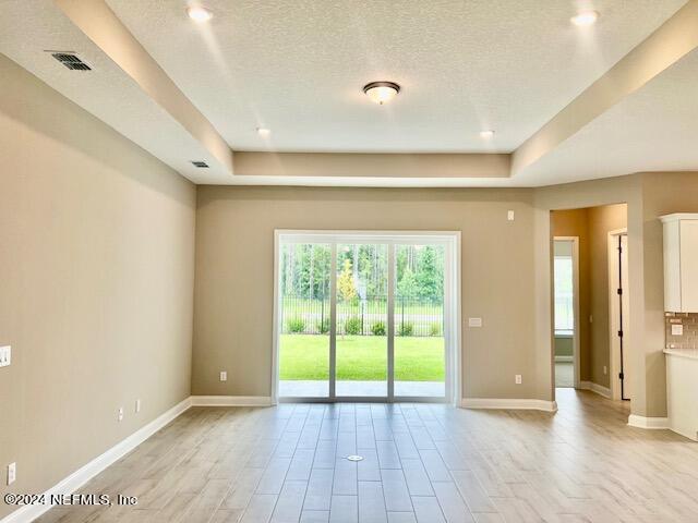 spare room featuring a textured ceiling, a tray ceiling, and light hardwood / wood-style floors