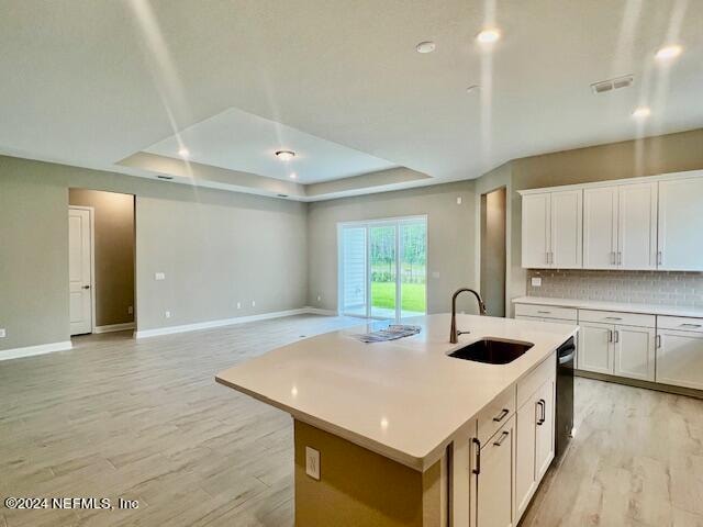 kitchen featuring an island with sink, white cabinetry, light wood-type flooring, dishwasher, and sink