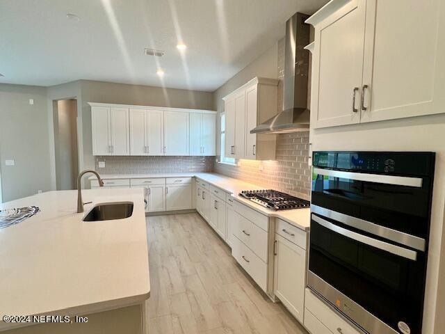 kitchen featuring wall chimney exhaust hood, sink, white cabinets, appliances with stainless steel finishes, and tasteful backsplash