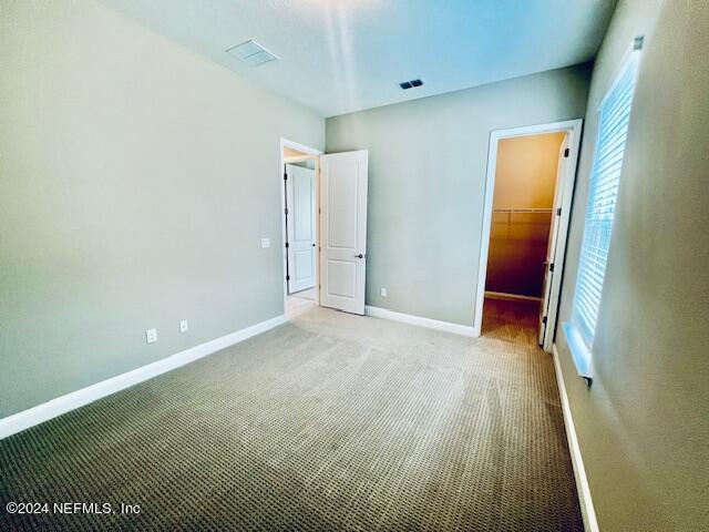 unfurnished bedroom with a spacious closet, a closet, and carpet